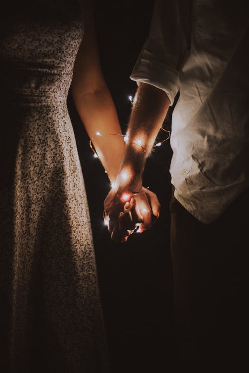 A pair of hands being held with lights wrapped around them