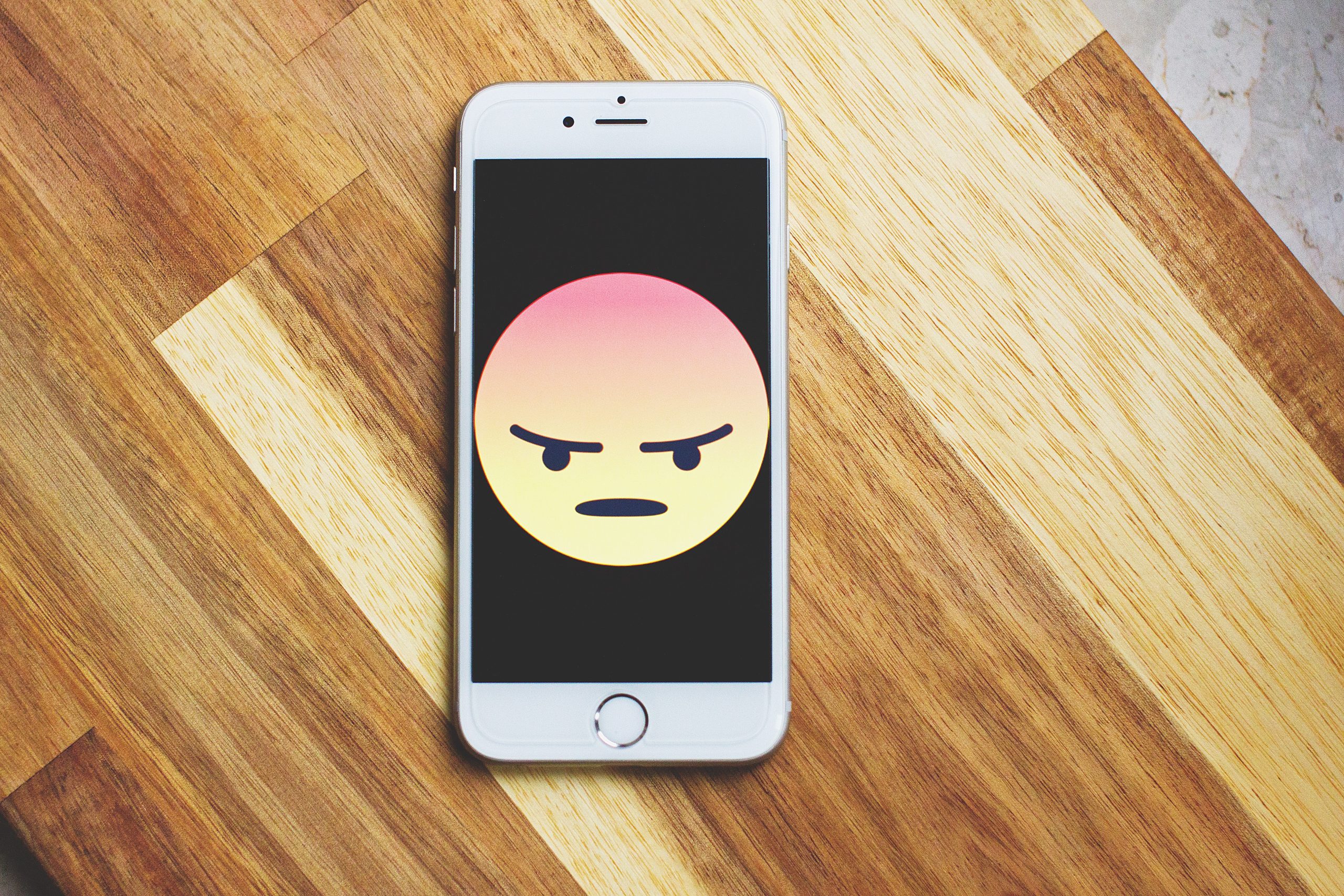 Smartphone with large anger emoji on the screen.
