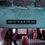 A sign on a brick wall that says, "Mind your head."