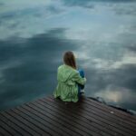 Girl sitting at the edge of a dock facing still water