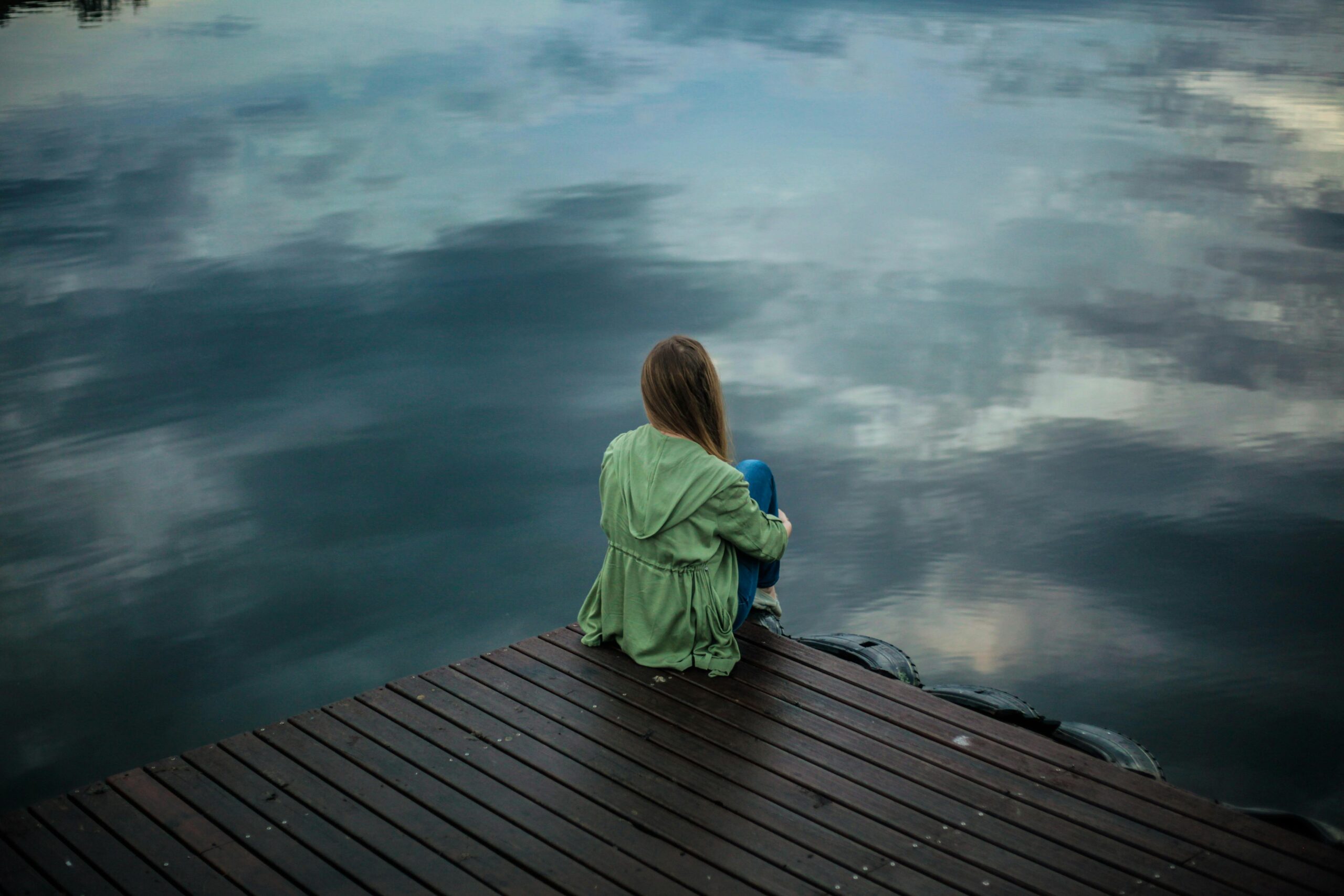 Girl sitting at the edge of a dock facing still water