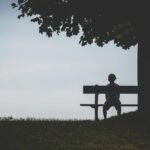 shadowy silhouette of a youth sitting on a bench at a ark